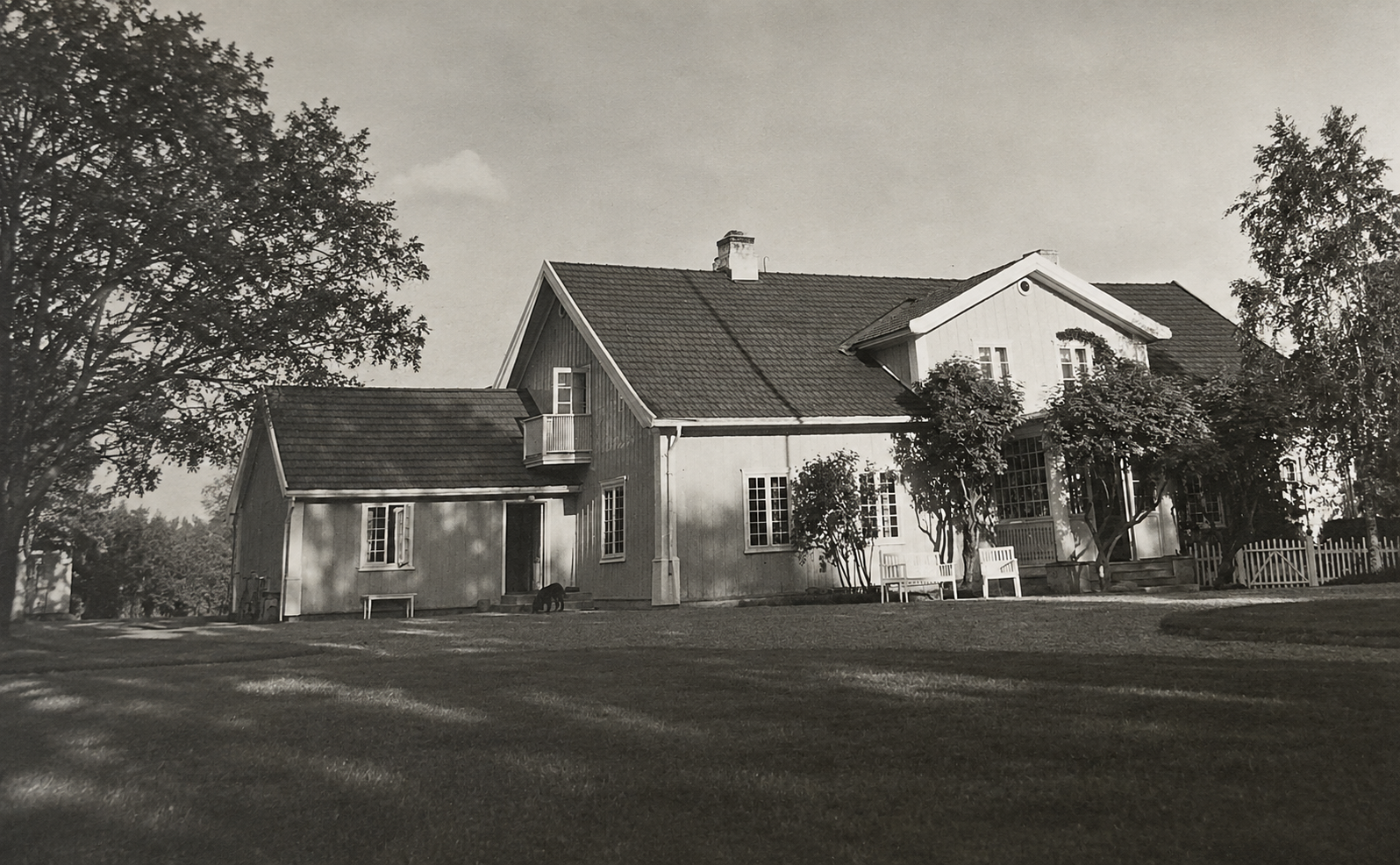 Historisk svart-hvitt fotografi av våningshuset med hage og trær