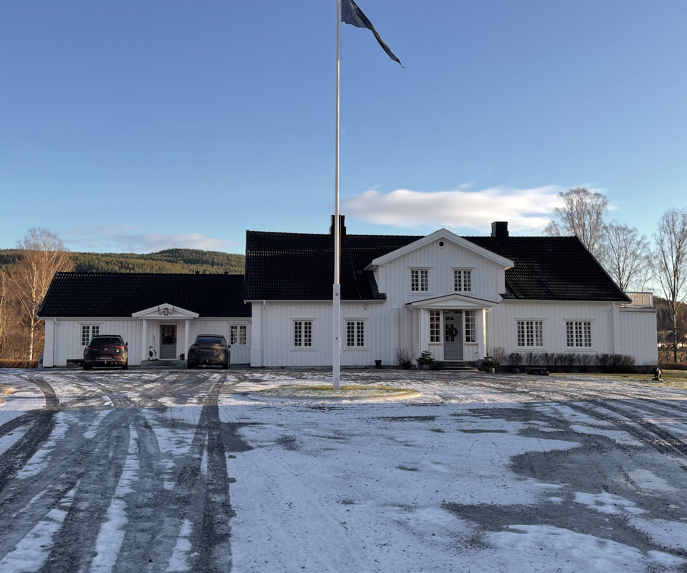 Våningshuset sett rett forfra fra tunet med flaggstang en vinterdag