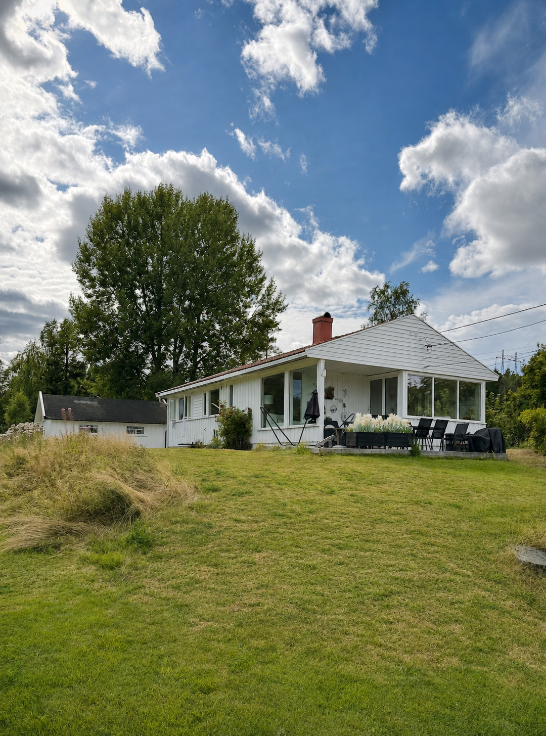 Eksisterende hvitt hus med hage og terrasse under blå himmel
