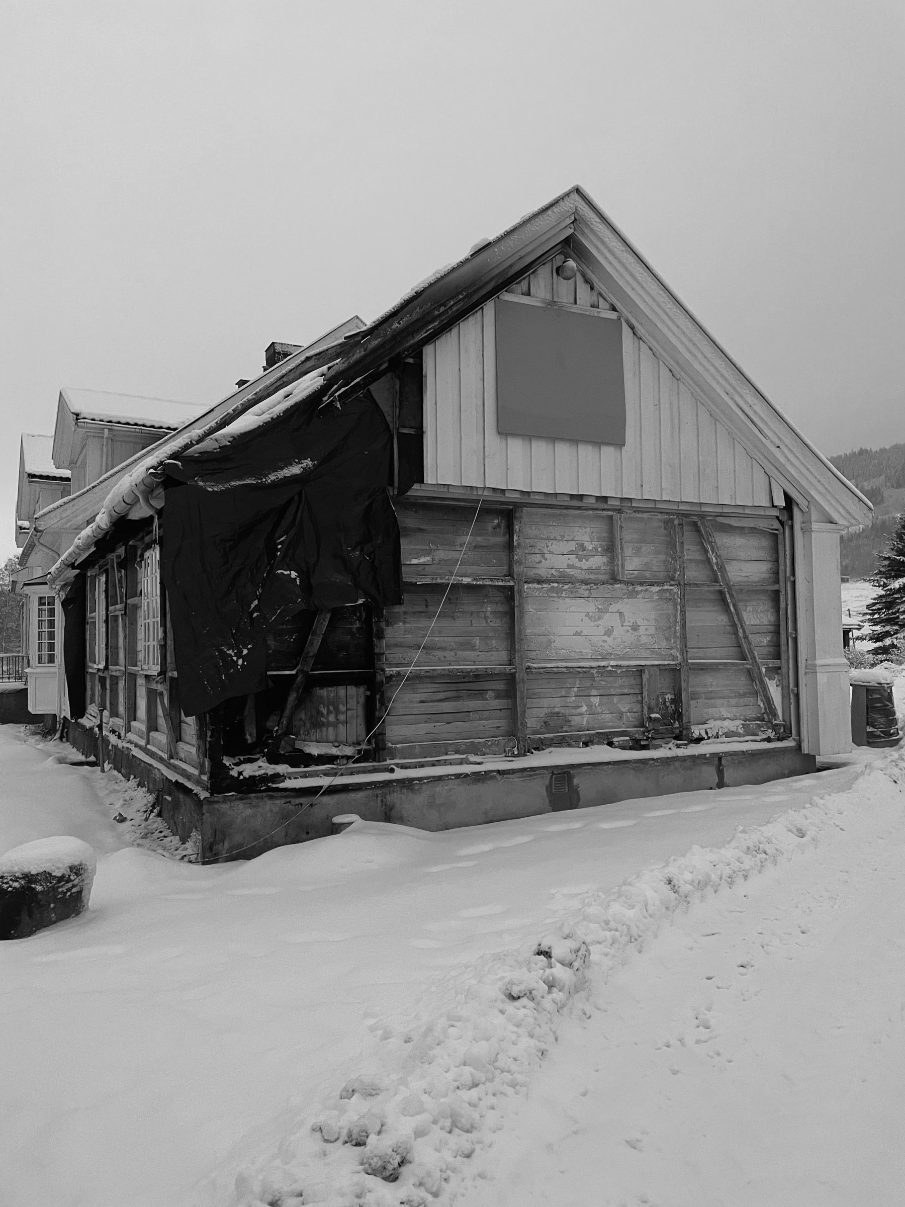 Brannskadet gavlvegg med avdekket laftverk og presenning