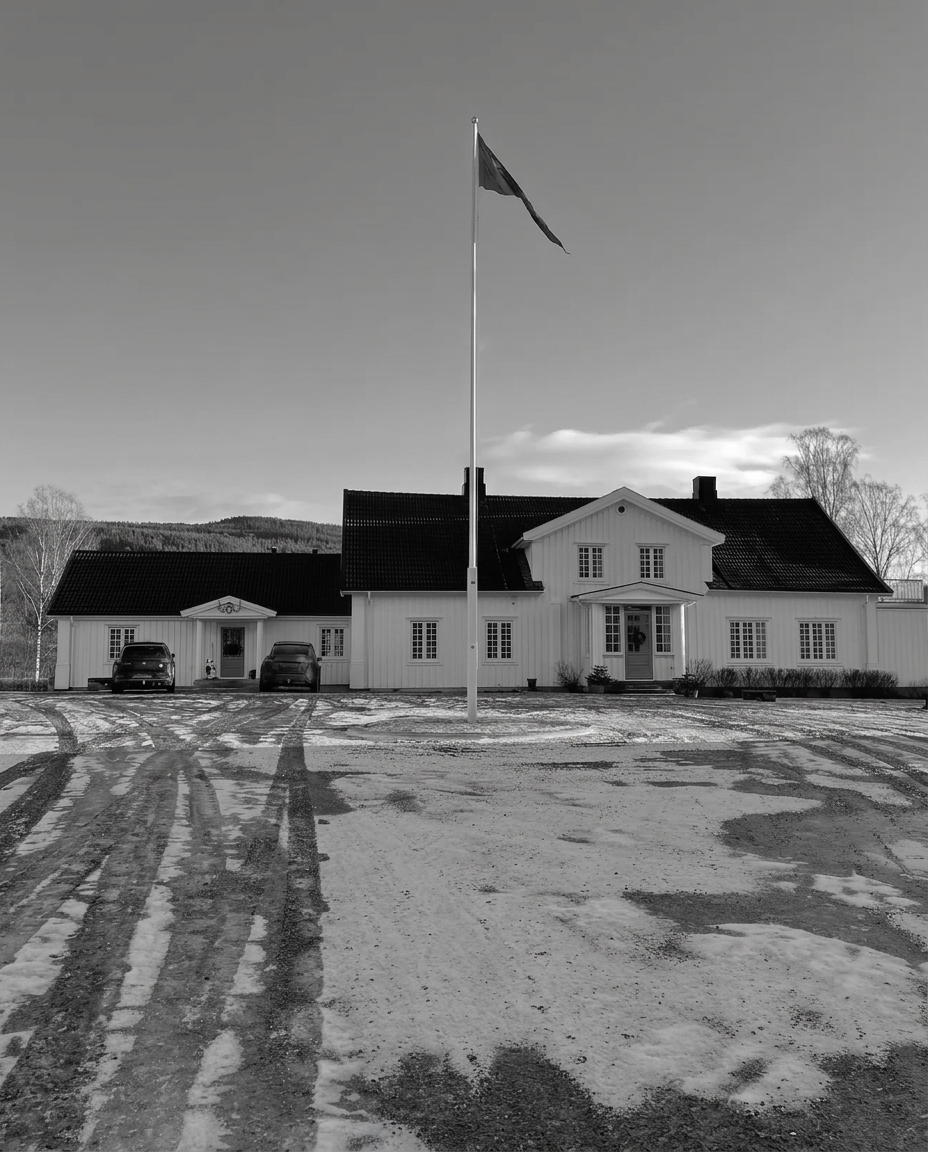 Våningshuset i svart-hvitt sett rett forfra fra tunet med flaggstang